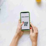 A person using a smartphone for grocery delivery surrounded by fresh fruits and vegetables., tags: moderne und - pexel