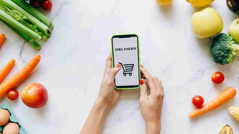 A person using a smartphone for grocery delivery surrounded by fresh fruits and vegetables., tags: moderne und - pexel